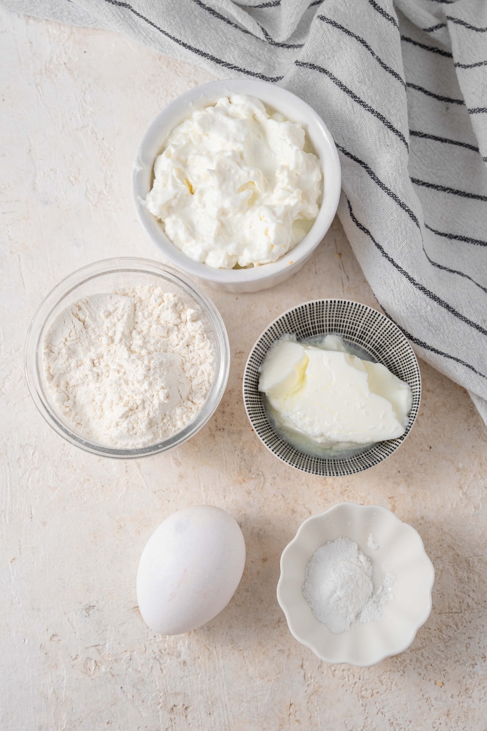 An overhead shot of several bowls of various sizes containing ingredients for cottage cheese waffles including cottage cheese, flour, greek yogurt, and an egg.