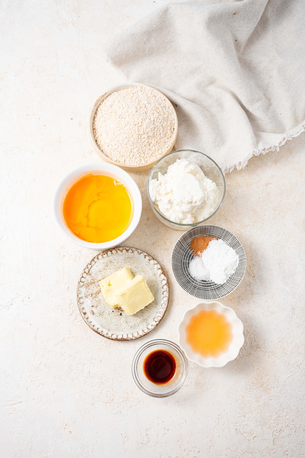 Bowls of cottage cheese, eggs, agave syrup, vanilla extract, oat flour, cinnamon, baking powder, salt, and butter.