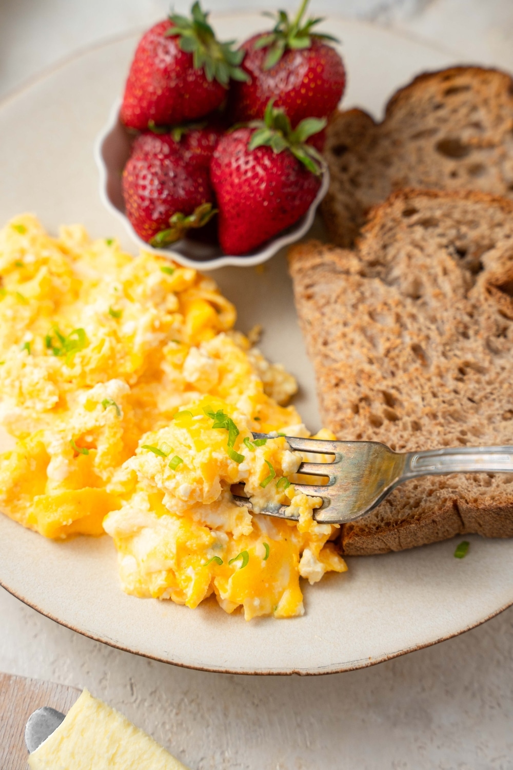 A fork digging into a cottage cheese omelet served with strawberries and toasted whole wheat bread slices.