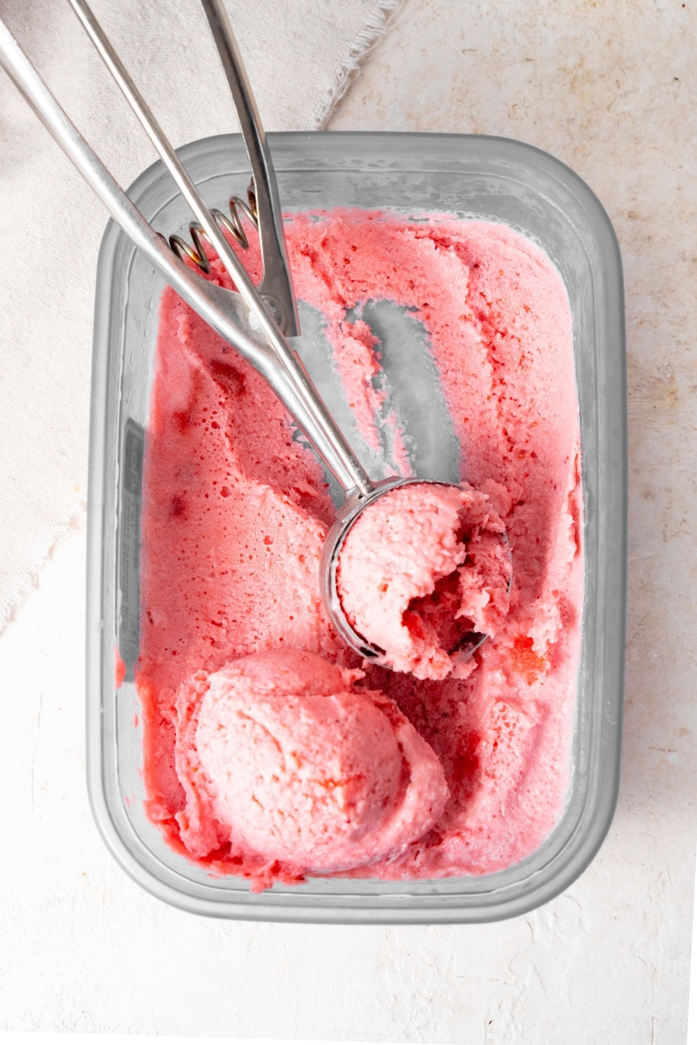 An ice cream scoop in a tub of strawberry cottage cheese ice cream