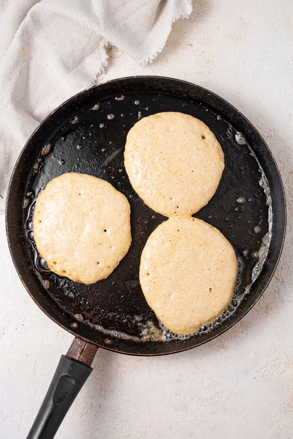 Three partially cooked pancakes on a cast iron skillet.