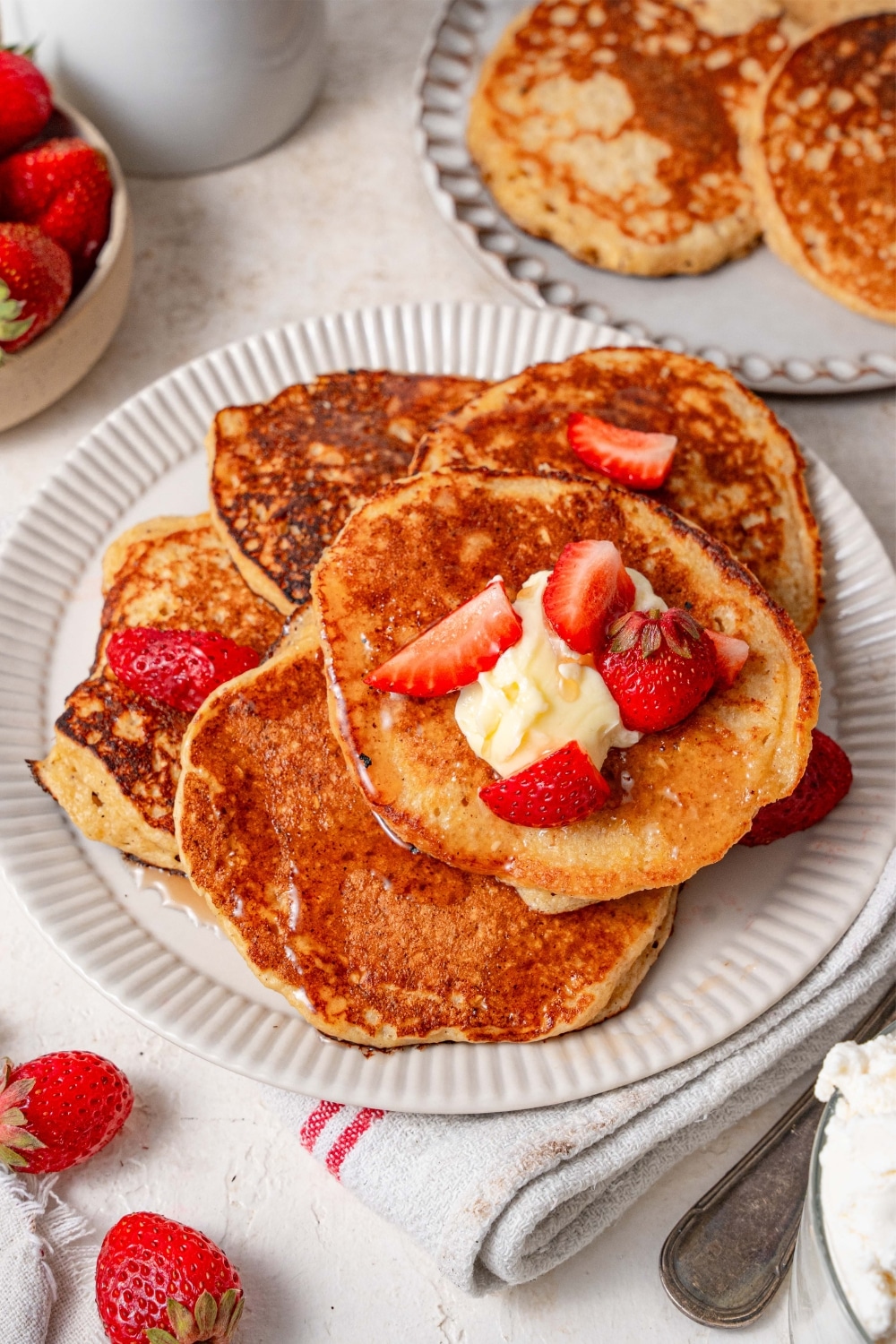 Five cottage cheese pancakes on a plate, topped with butter and strawberry slices.