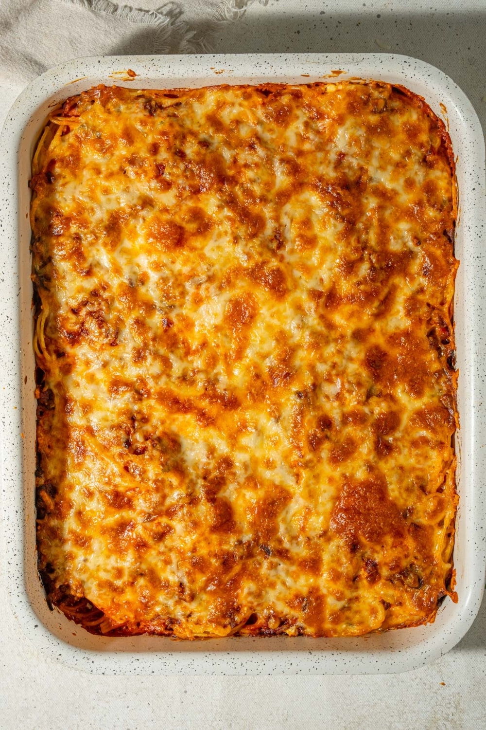 A casserole dish of baked spaghetti topped with golden melted cheese.