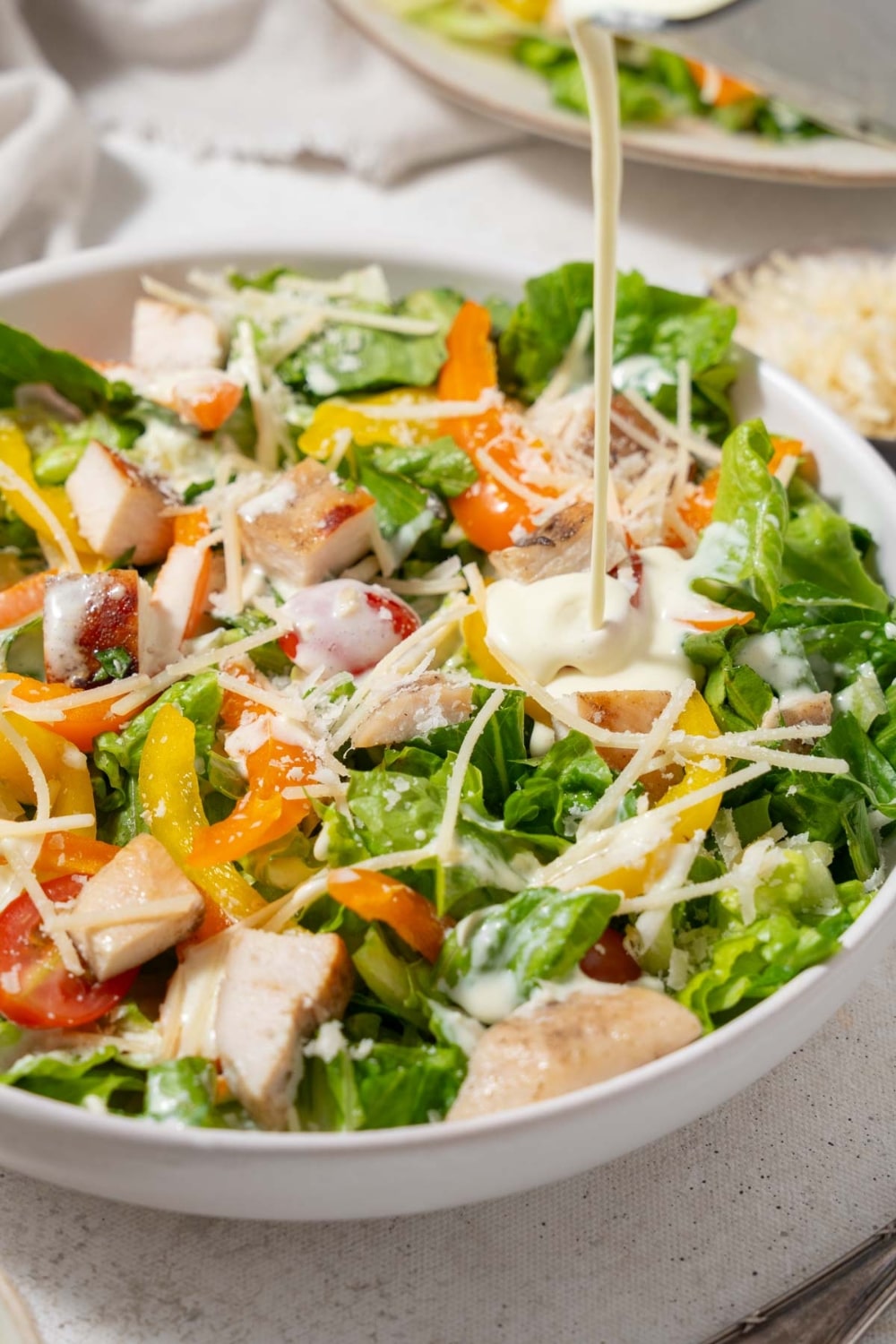 Dressing being poured onto a chicken Caesar salad.