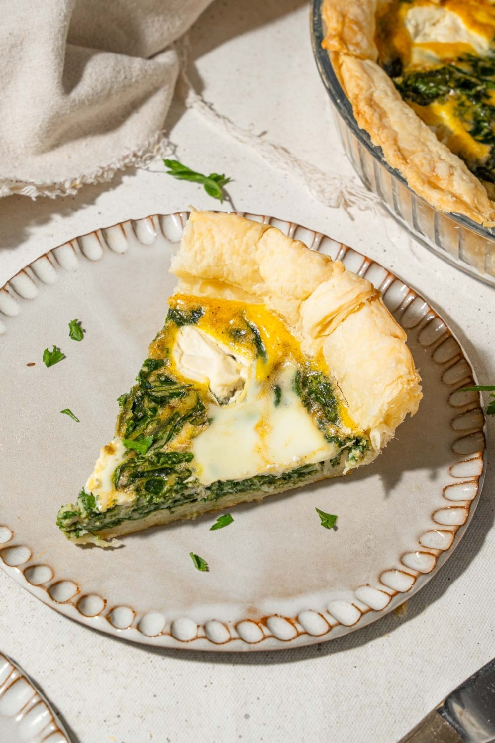A slice of spinach quiche with whipped cottage cheese topping on a plate, garnished with fresh herbs.