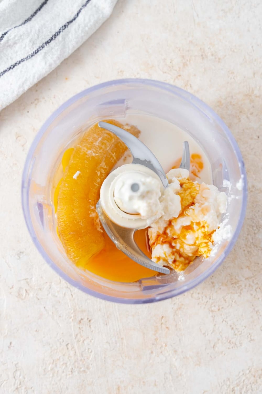 A banana, egg, cottage cheese, vanilla extract, almond milk, and maple syrup in a food processor.