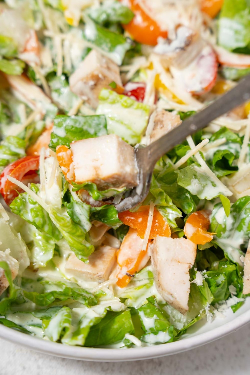 Scooping chicken Caesar salad with a fork.