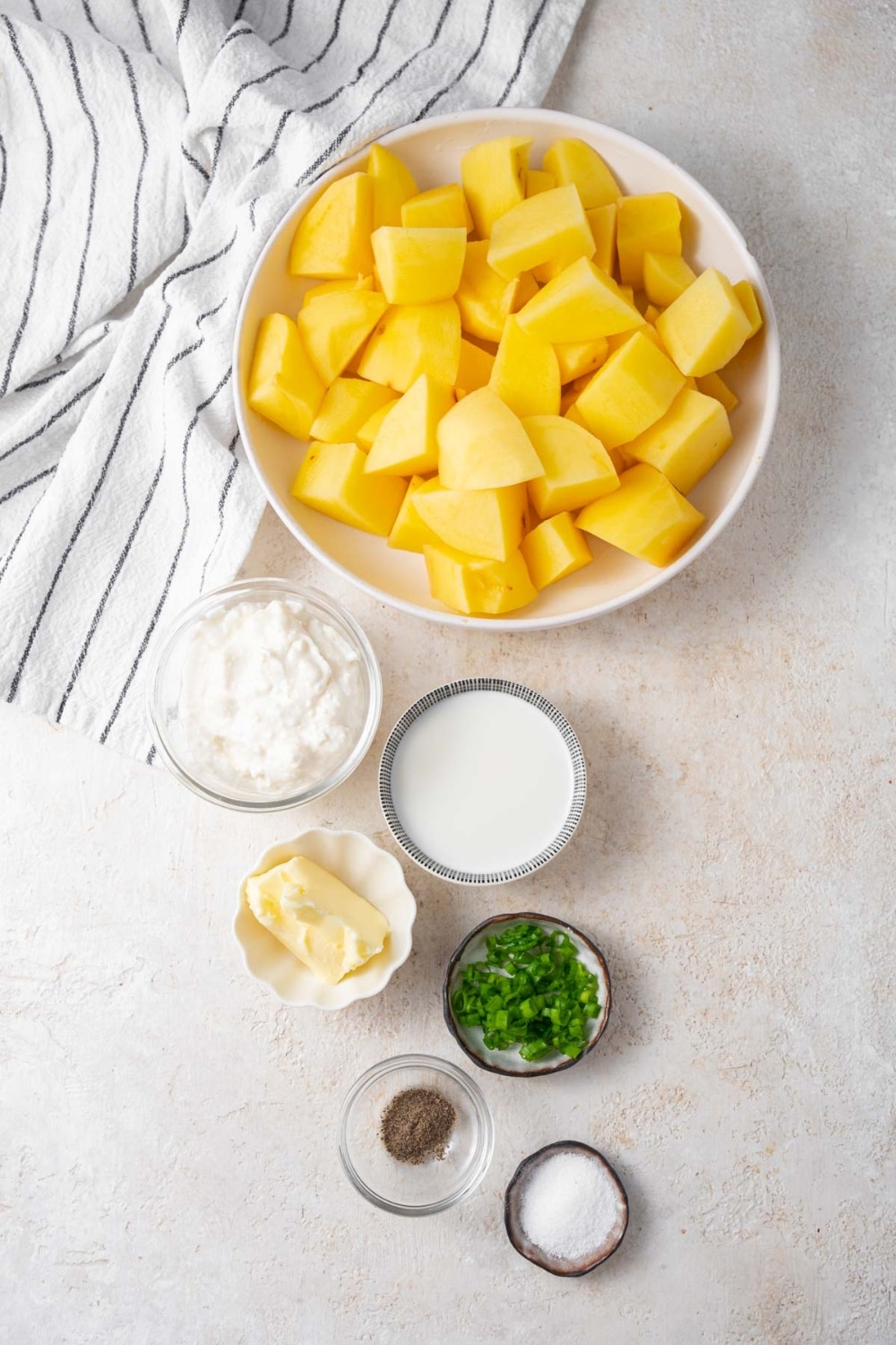 Bowls of peeled and quartered potatoes, cottage cheese, 2% milk, butter, chopped chives, salt, and pepper.