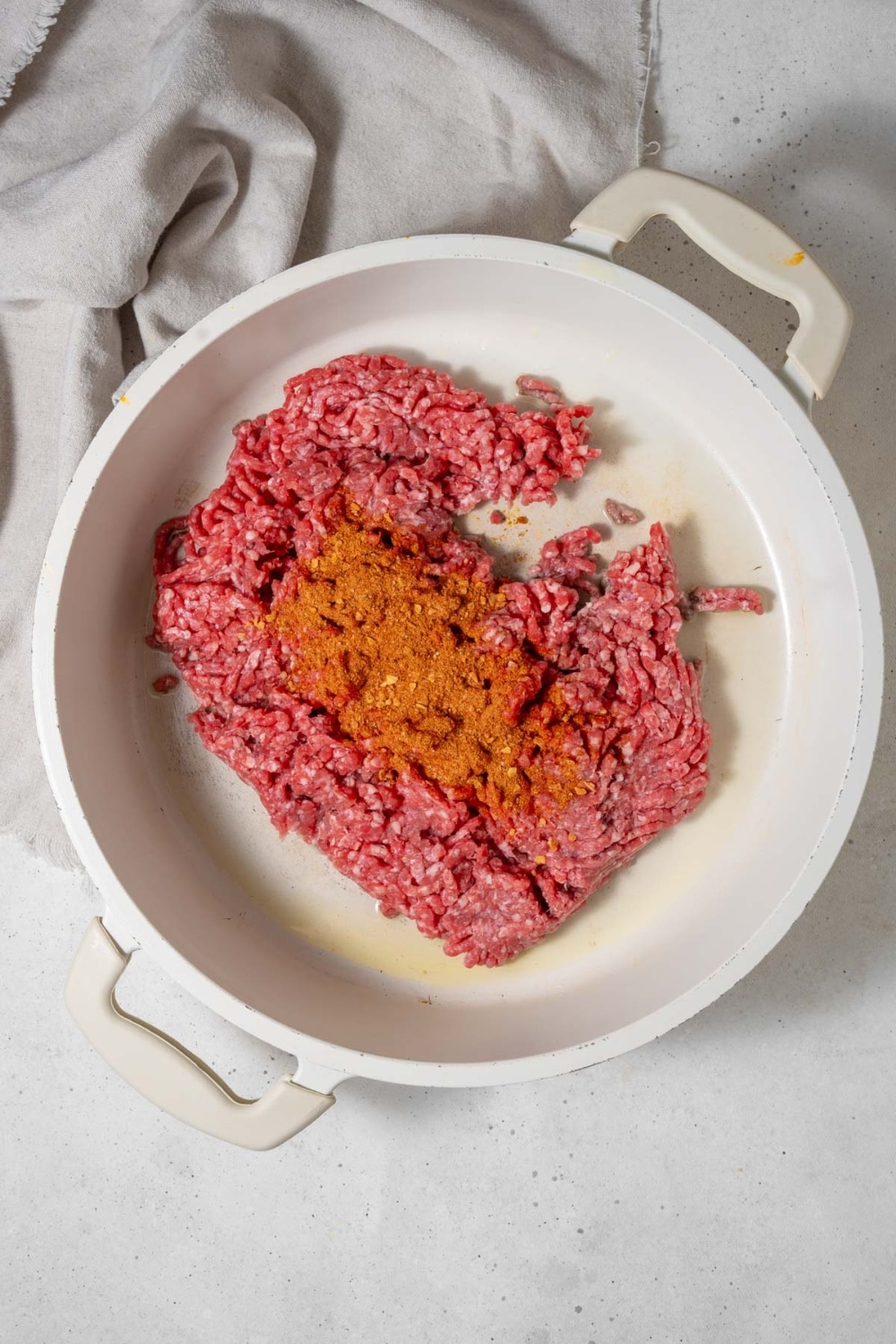 Raw ground beef and spices in a white pot.