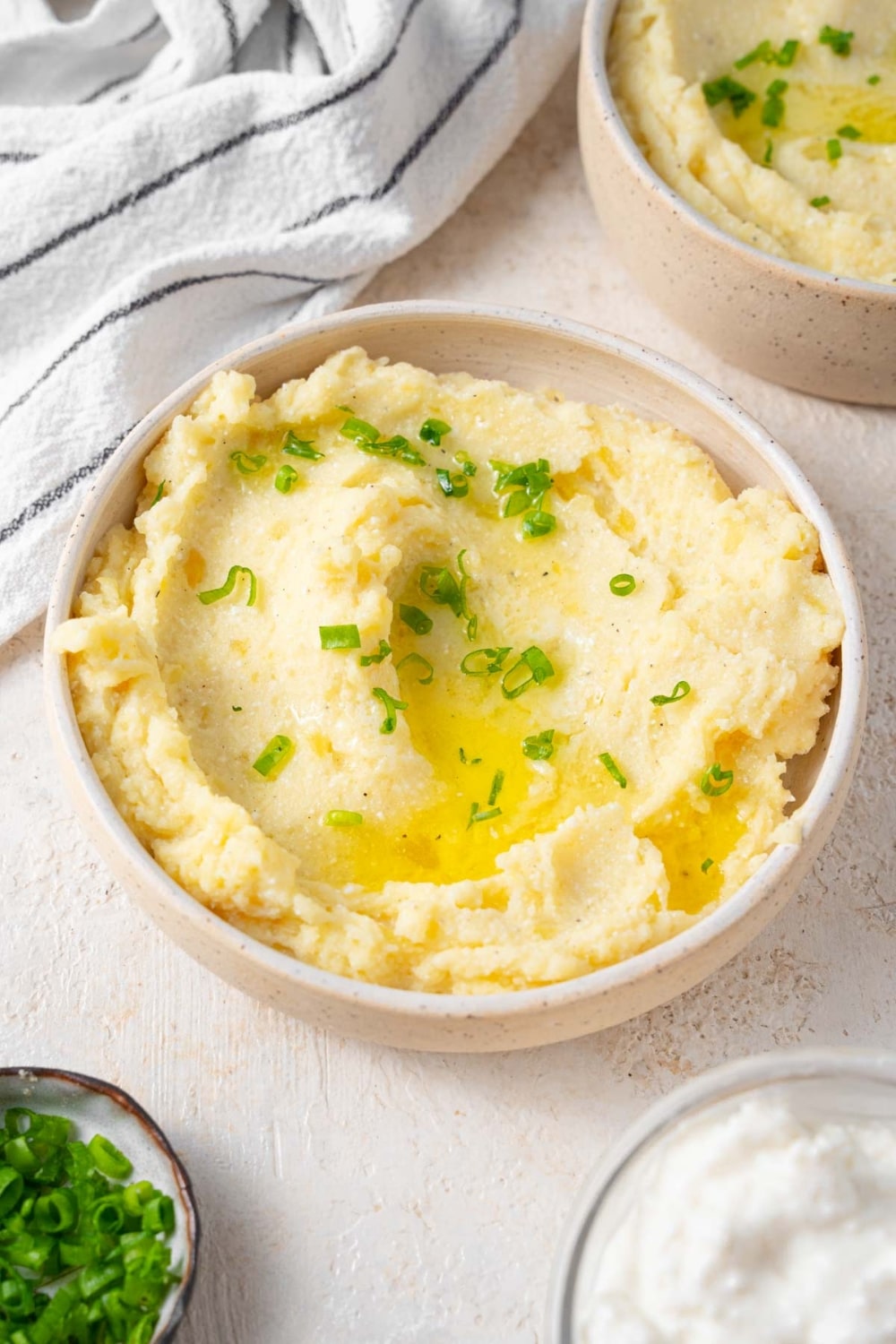 A bowl of cottage cheese mashed potatoes garnished with chives and melted butter.