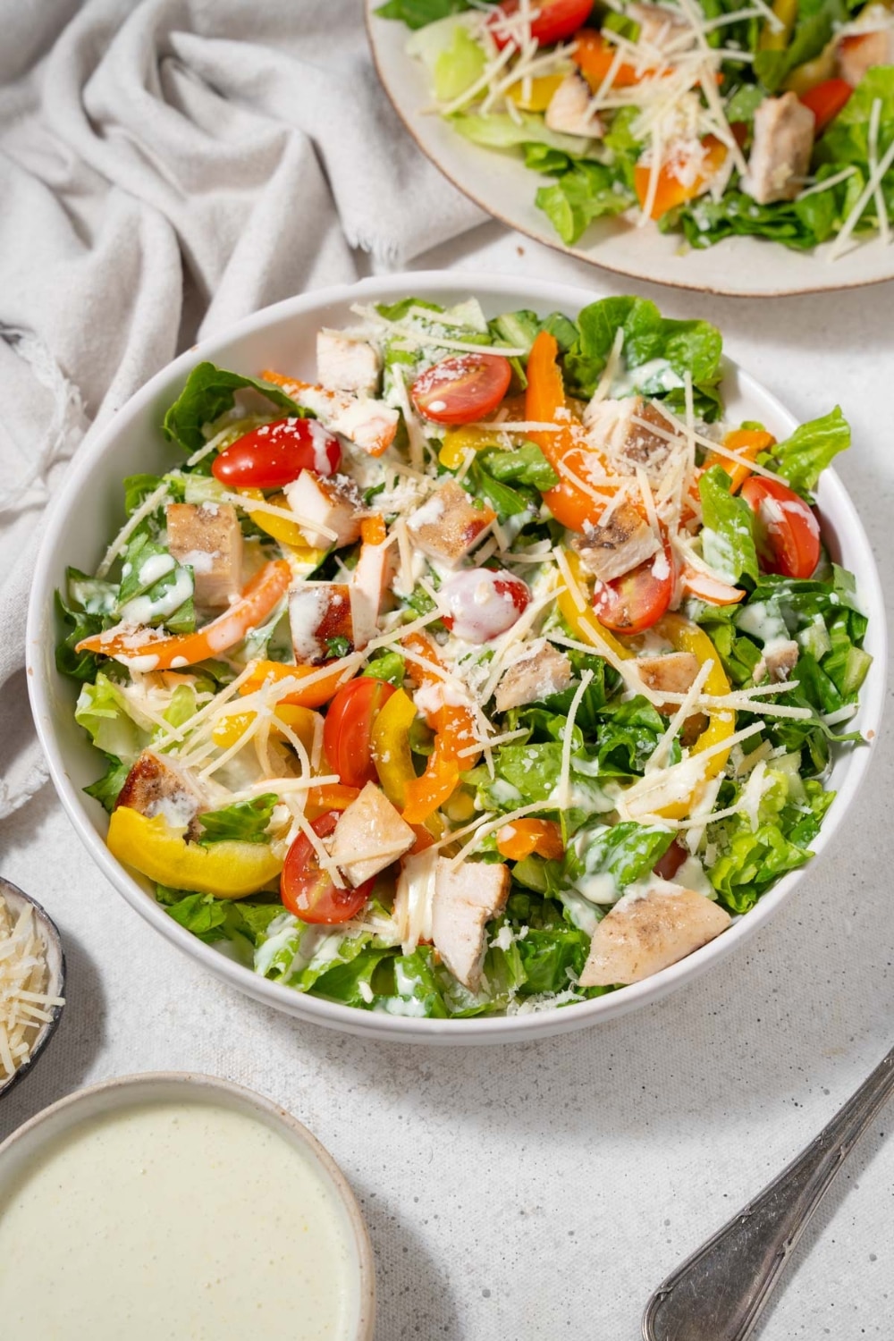 Chicken Caesar salad in a bowl topped with grated parmesan cheese and dressing.