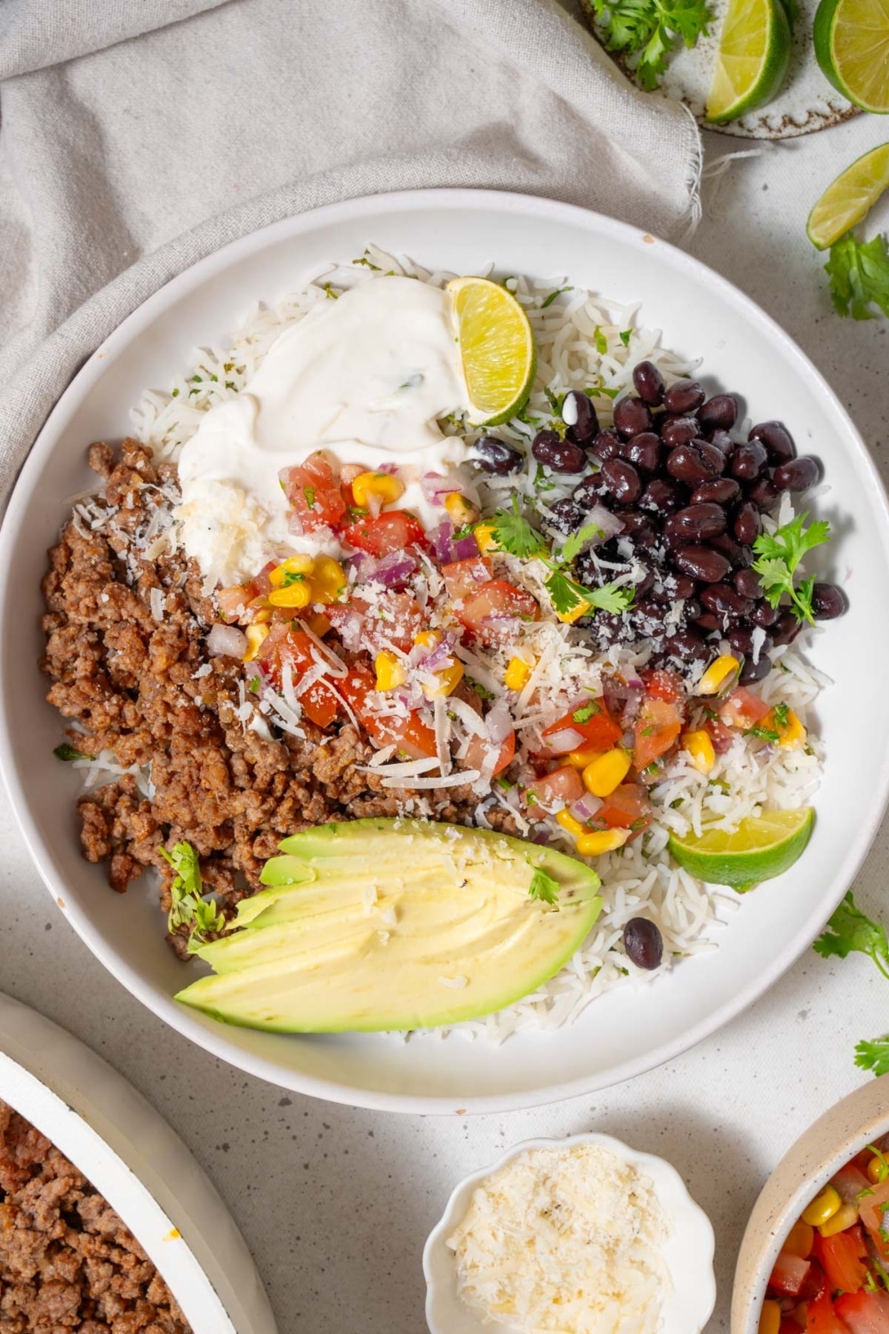 Top view of a taco bowl with cilantro lime rice, black beans, taco meat, corn salsa, sliced avocado, lime, and cottage cheese sauce.