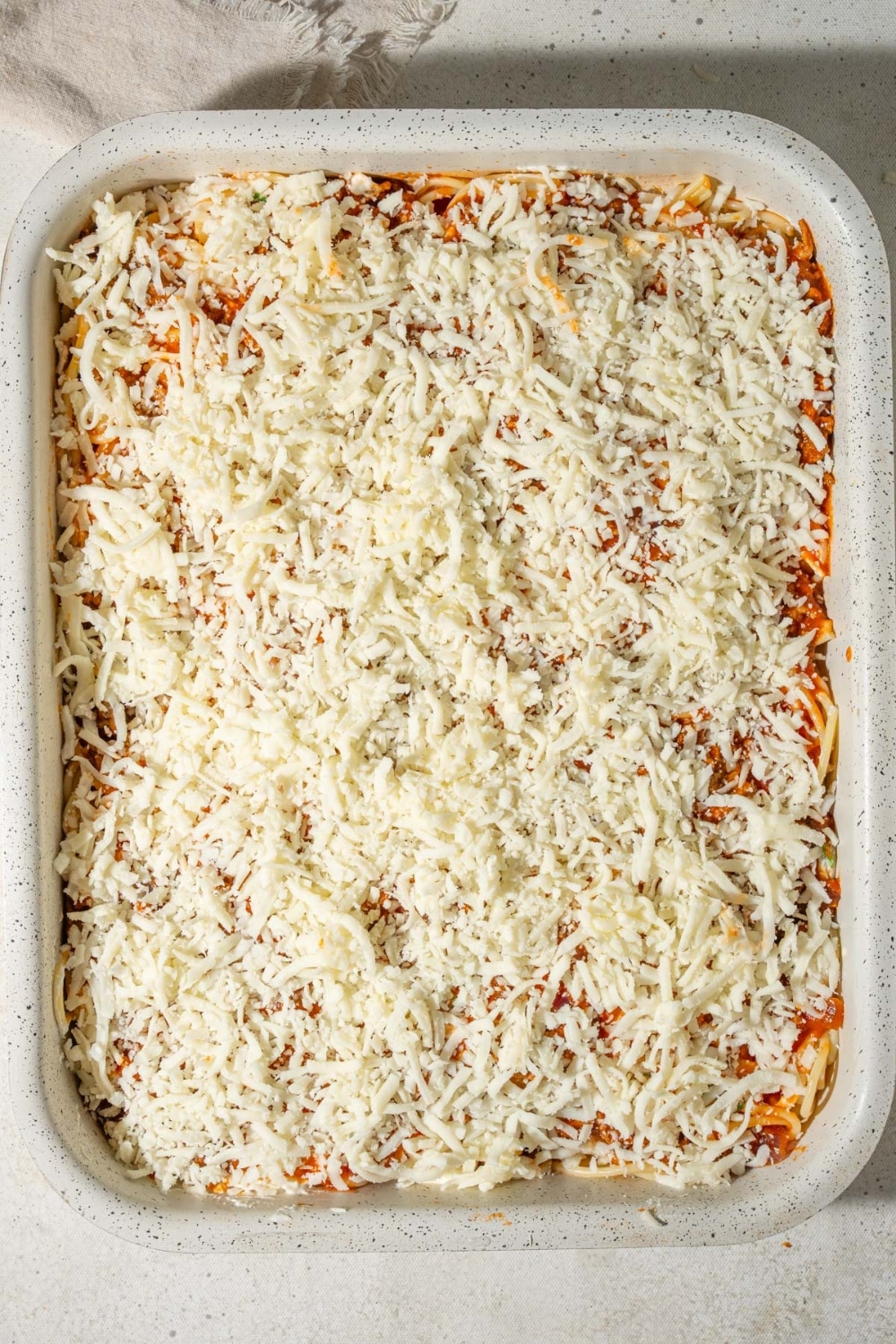 Spaghetti topped with shredded mozzarella cheese in a casserole dish.