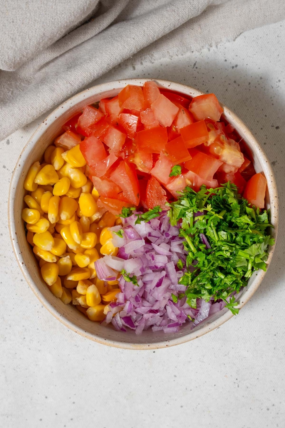 A bowl of corn kernels, minced red onion, chopped cilantro, and diced tomatoes.